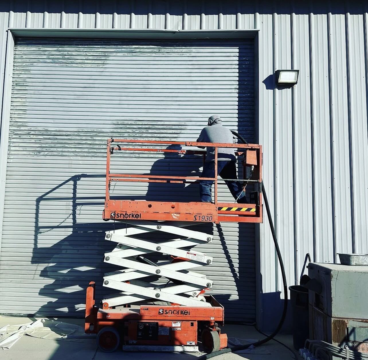 Worker on a scissor lift blasting a commercial roll-up door